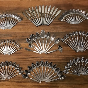 May include: A set of silverware arranged in a fan shape on a wooden surface. The set includes forks, knives, and spoons.