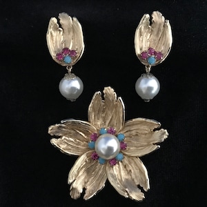May include: A gold flower brooch with a pearl in the center and pink and blue rhinestones. Matching earrings with a pearl drop and pink and blue rhinestones.