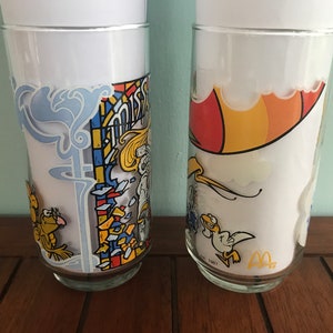 May include: Two vintage McDonald's glasses with cartoon characters. The first glass features a stained glass design with a yellow bird and the text "Mister McFeely". The second glass features a yellow bird flying with a red and yellow umbrella.