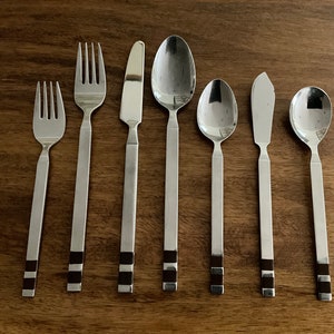 May include: Set of eight silver-toned flatware with black accents. The set includes two forks, two spoons, a butter knife, and three spoons.