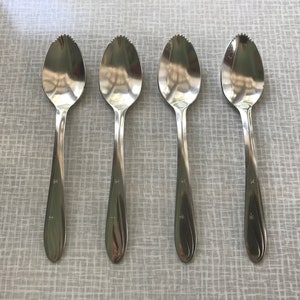 May include: Four silver citrus spoons with serrated edges. The spoons have a curved handle and are arranged in a row.