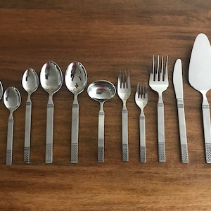May include: A set of silverware with a decorative pattern on the handles. The set includes spoons, forks, a serving spoon, and a cake server.