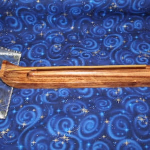 May include: A wooden incense holder with a natural finish. The holder is rectangular with a curved end and a groove to hold the incense stick. A lit incense stick is placed in the holder. The background is a blue fabric with a swirling pattern.