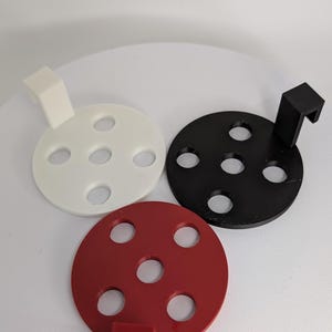 May include: Three circular, multi-holed objects in white, black, and red. Each has a small, rectangular handle. The objects are arranged on a white surface. The design is simple and modern.