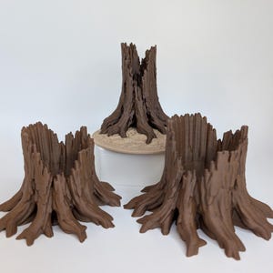 May include: Three brown, hollow tree stump replicas with textured, jagged bark surfaces. Two stumps are positioned in the foreground, while the third is elevated on a circular base in the background. Each piece features a wide, root-like base.