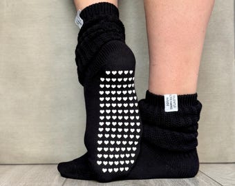 Puede incluir: Calcetines negros de punto con agarres blancos en forma de corazón en las suelas. Los calcetines están arrugados alrededor de los tobillos y tienen una etiqueta que dice "SILENTLY SCREAMING INSIDE".