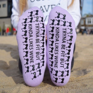 May include: Purple socks with black wine glass designs and the text "Tryna be fit but kinda likes wine" on each sock.