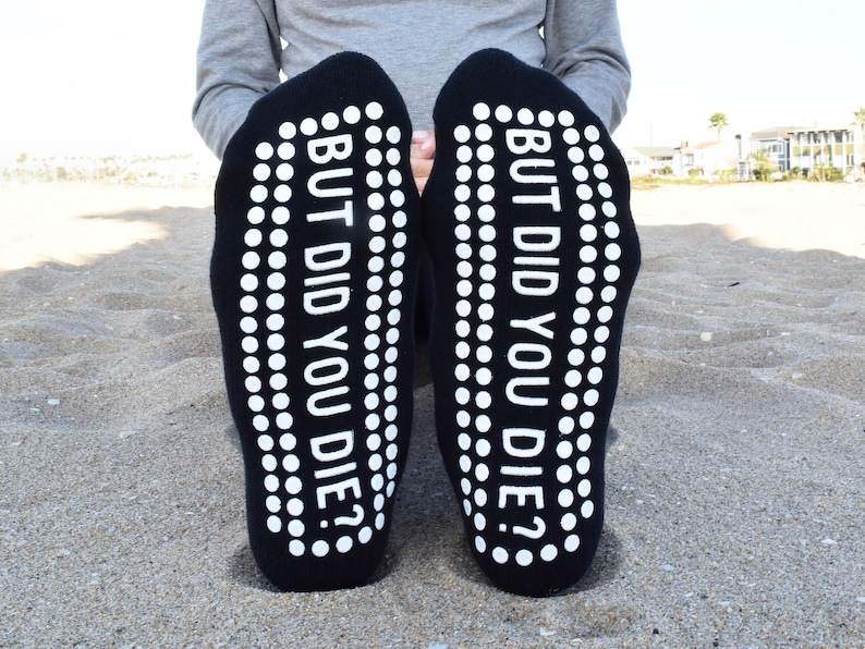 May include: A pair of black socks with white grip dots on the bottom. The socks have the text "BUT DID YOU DIE?" printed on the bottom.
