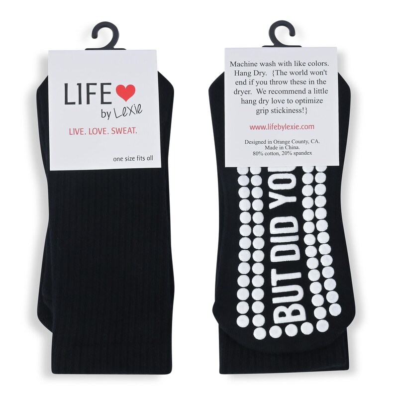 May include: A pair of black socks with white grip dots and the text "BUT DID YOU" on the bottom. The socks are packaged with a white card that says "LIFE by Lexie LIVE. LOVE. SWEAT. one size fits all".