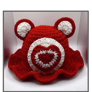 May include: A red and white crochet bucket hat with bear ears and a heart patch. The hat is handmade and features the text "All My Heart Bear Bucket Hat Patch Crochet Pattern".