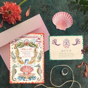 May include: A wedding invitation suite featuring a seashell and seahorse design. The suite includes an invitation, RSVP card, and pink envelope. A ring and seashell are also present, with floral accents.