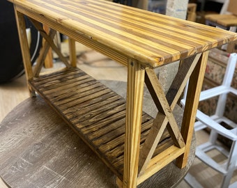 May include: A wooden console table with a slatted top and a lower shelf. The table has an X-shaped support on each end. The wood has a natural finish with varying shades of light and dark brown.