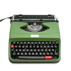 Peut inclure: Une machine à écrire vintage verte avec un clavier noir et des touches rouges. La machine à écrire a un levier de retour chariot argenté et un rouleau argenté.