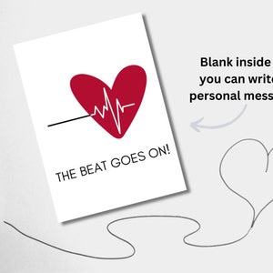 May include: A white card with a red heart and a black line with a white EKG line running through it. The text "THE BEAT GOES ON!" is printed below the heart. The card is blank inside for writing a personal message.