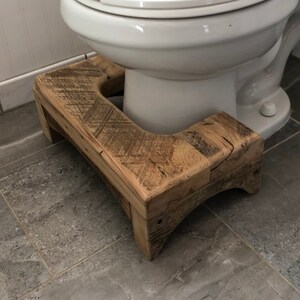 May include: A wooden toilet step stool with a rustic finish. The stool is made of reclaimed wood and has a natural wood grain. The stool is placed in front of a white toilet.