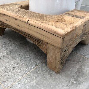 May include: A wooden toilet seat riser with a natural wood finish. The riser has a curved top and two legs on each side.