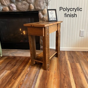 May include: A rustic wooden end table with a shelf, featuring a natural wood finish and a polycrylic top coat. The table is in front of a fireplace with a stone surround.
