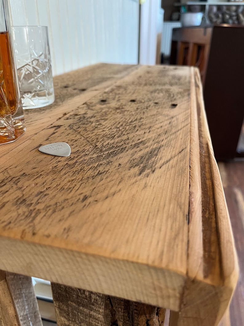 May include: Close-up of a rustic wooden table top with a worn, natural finish. The table has a slightly rounded edge and a guitar pick is resting on the surface.