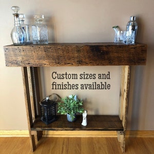 May include: A rustic wooden console table with a shelf. The table has a dark brown stain and is made of reclaimed wood. The table is 30 inches tall and 36 inches wide. Custom sizes and finishes are available.