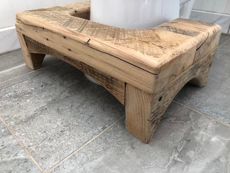 May include: A wooden toilet seat riser with a natural wood finish. The riser has a curved top and two legs on each side.