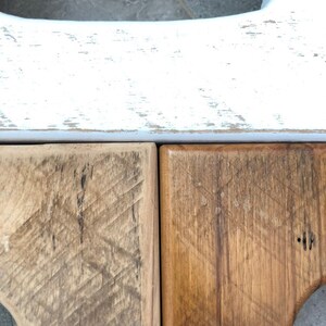 May include: Close-up of two wooden surfaces, one stained a light brown and the other a darker brown. The top surface is painted white with a distressed finish.