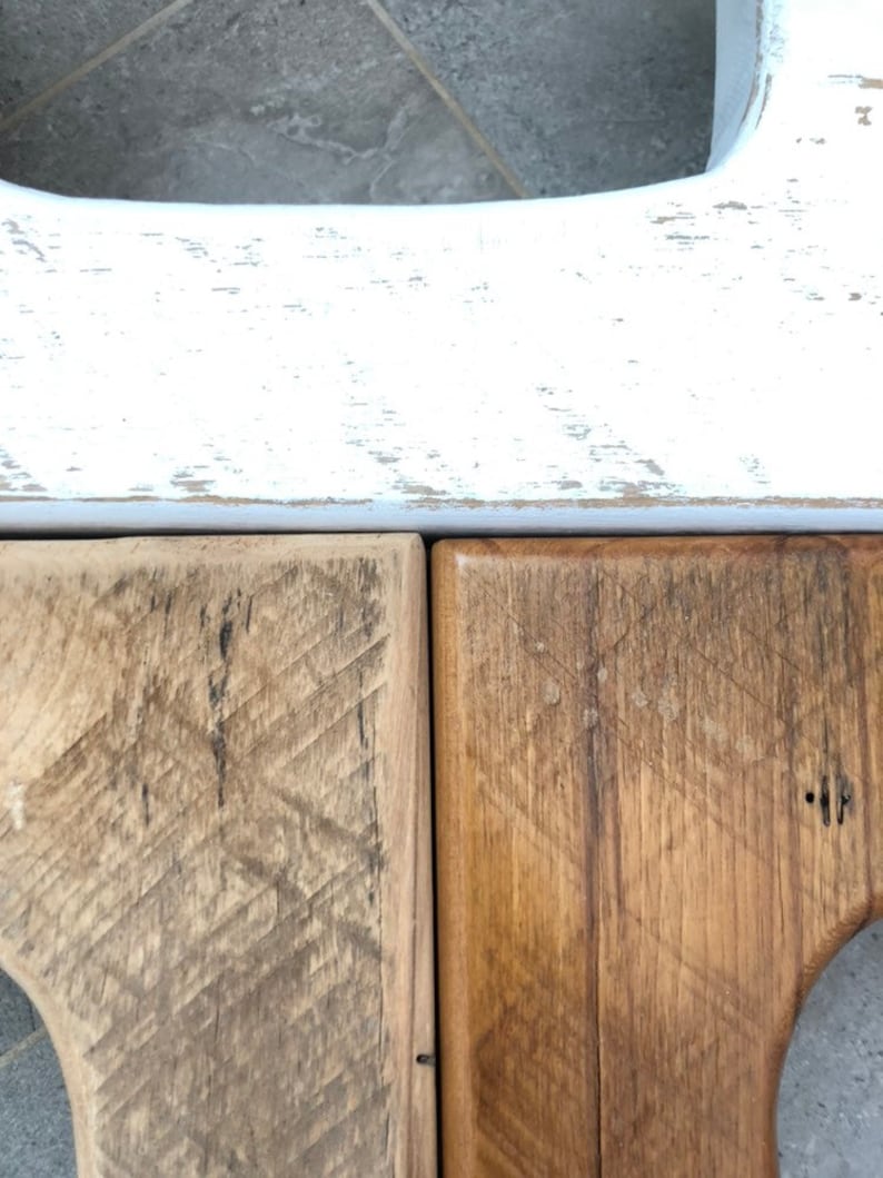 May include: Close-up of two wooden surfaces, one stained a light brown and the other a darker brown. The top surface is painted white with a distressed finish.