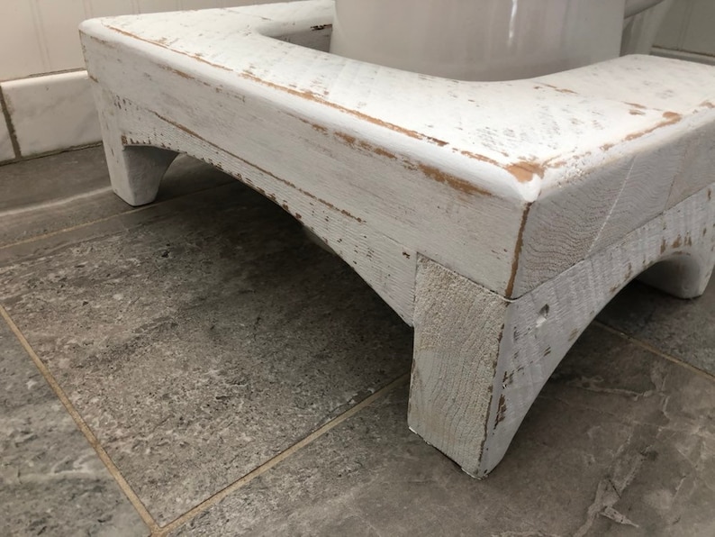 May include: White wooden stool with a distressed finish. The stool has a curved base and is designed to be used as a step stool.
