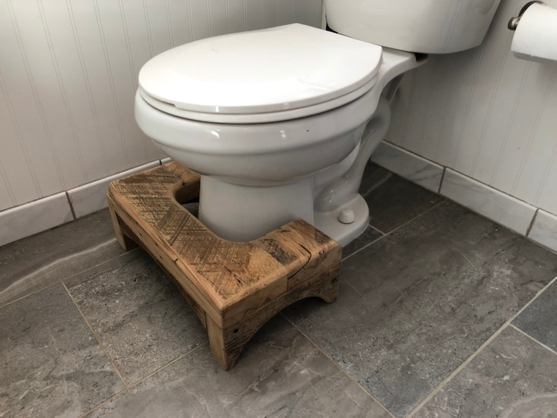 May include: A wooden toilet step stool with a rustic finish. The stool is made of reclaimed wood and has a natural wood grain. The stool is placed in front of a white toilet.