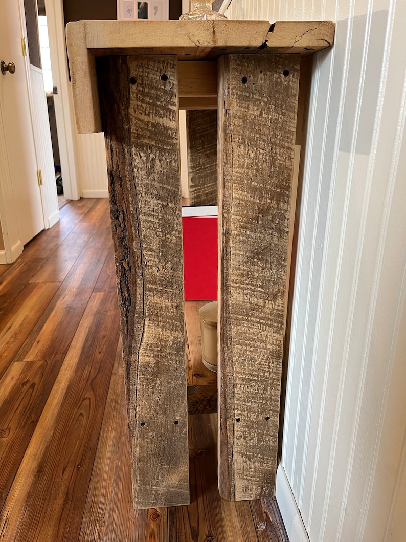 May include: A rustic wooden console table with a natural wood finish. The table has a simple design with two legs and a rectangular top. The table is made of reclaimed wood and has a distressed look.