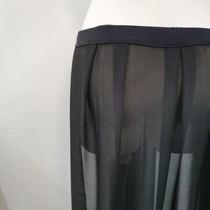 May include: A black skirt featuring a sheer, semi-transparent fabric with vertical pleated panels. The garment has a solid, opaque waistband and a flowing, lightweight construction that hangs straight down from the waistline.
