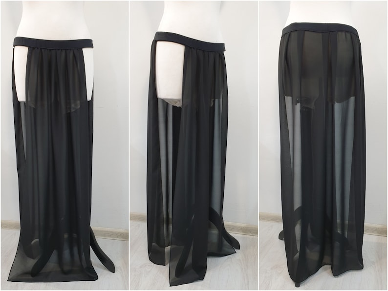 May include: A floor-length black skirt made of sheer, translucent fabric. The garment features a wide, solid black waistband and high side slits that extend from the waist to the hem, creating an open, flowing silhouette with layered panels.
