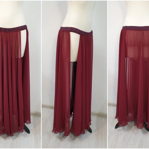 May include: A floor-length, sheer burgundy skirt featuring a dark maroon elastic waistband and high side slits that reveal the legs. The garment is made of a lightweight, flowing chiffon-like fabric that drapes down to the ankles in soft pleats.