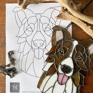 May include: Stained glass dog portrait with brown, white, and pink accents. The dog's face is detailed with a black nose and a pink tongue. A black and white line drawing of the dog is next to the stained glass piece.