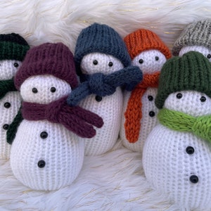 May include: Six knitted snowman ornaments with different colored hats and scarves. The snowmen are white with black eyes and buttons. The hats are green, purple, blue, orange, green, and gray. The scarves are green, purple, blue, orange, green, and gray.