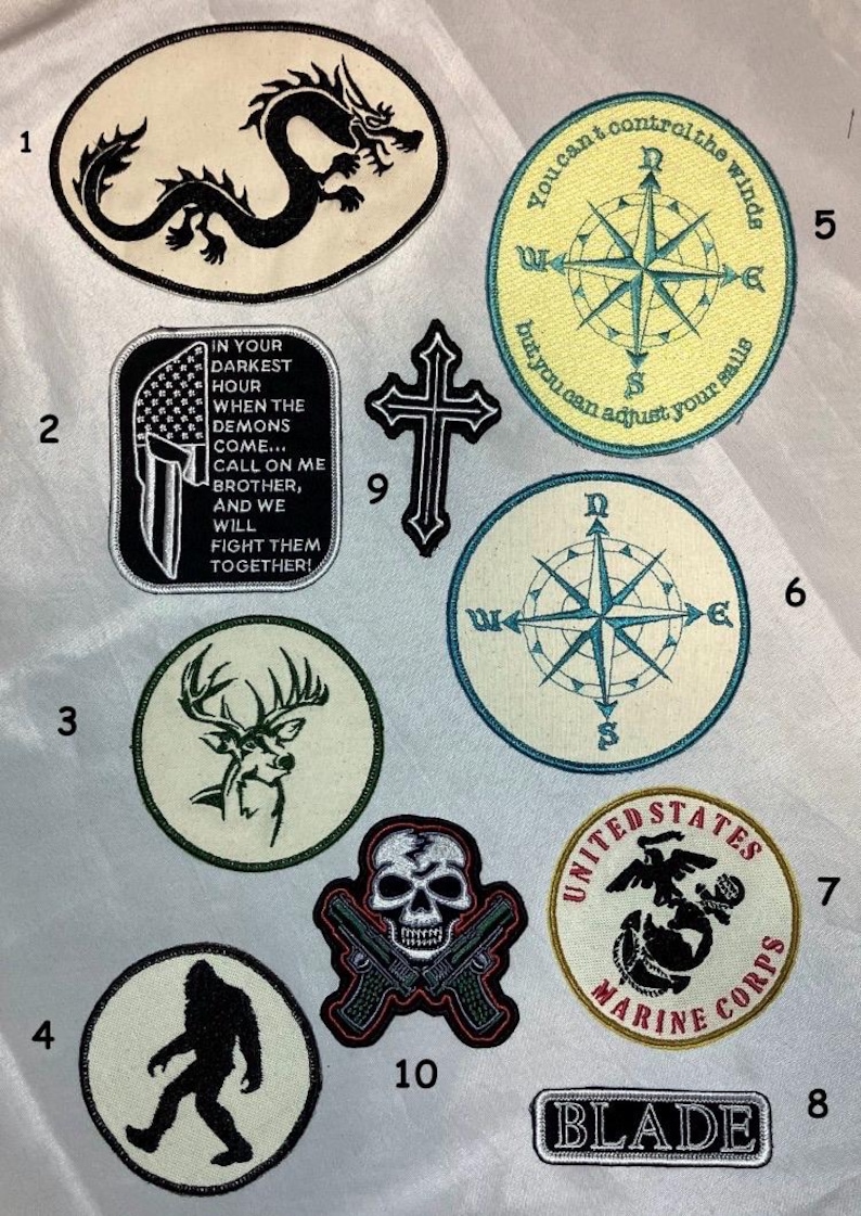 May include: A collection of ten embroidered patches featuring various designs including a black dragon, a Spartan helmet with text, a deer head, a Bigfoot silhouette, compasses, a cross, a skull with pistols, a Marine Corps emblem, and the word BLADE.