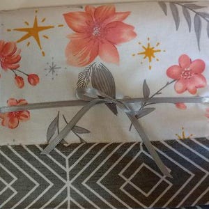 May include: A set of fabric squares with a floral pattern in shades of pink and white, tied together with a gray ribbon. The fabric squares have a geometric pattern in shades of gray and white on the back.