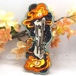May include: Embroidered patch featuring a stylized candle with flames in orange and yellow, surrounded by dark blue and teal accents. The patch has a unique design with the text ALEKIVZ.ETSY.COM.