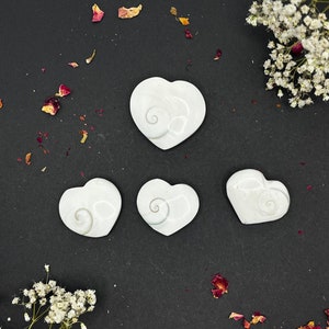 May include: Four white heart-shaped polished stones with a swirling pattern on a black background.