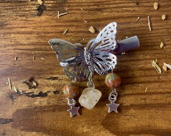 May include: Silver butterfly hair clip with three dangling charms: two brown and orange jasper beads and a clear quartz crystal. Each charm is attached to a silver star.
