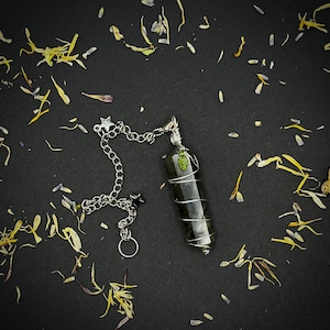 May include: A green crystal pendulum with a silver chain and a star charm. The pendulum is wrapped in wire and has a small green leaf charm.