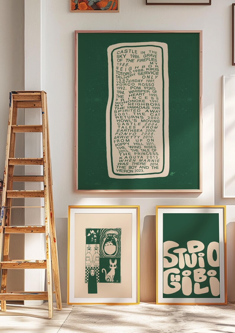 Puede incluir: Una colecci&oacute;n de impresiones art&iacute;sticas enmarcadas con temas de Studio Ghibli. Una impresi&oacute;n enumera los t&iacute;tulos de las pel&iacute;culas de Ghibli, otra muestra personajes y una tercera muestra las palabras "Studio Ghibi". Las impresiones tienen marcos dorados y se exhiben contra una pared blanca.