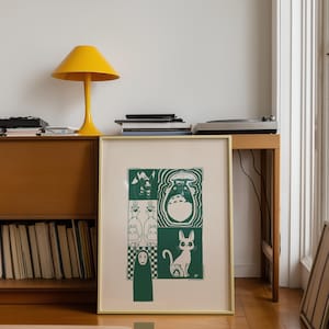 May include: A framed art print featuring green and white illustrations of characters from a popular animated film. The print is in a gold frame and is displayed on a wooden cabinet. A yellow lamp and a record player are also visible.