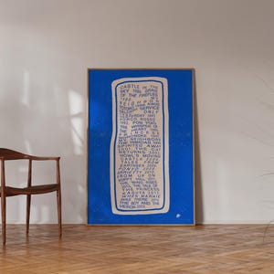 May include: A framed blue poster with white text. The text is a list of titles and dates. The poster is in a wooden frame and is leaning against a white wall. A wooden chair and a potted plant are in the background.