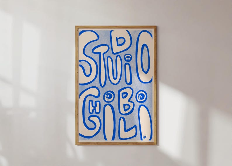 May include: A framed art print with the words "STUDIO GILI" in blue, stylized lettering on a light blue background. The artwork is in a wooden frame and hangs on a white wall.
