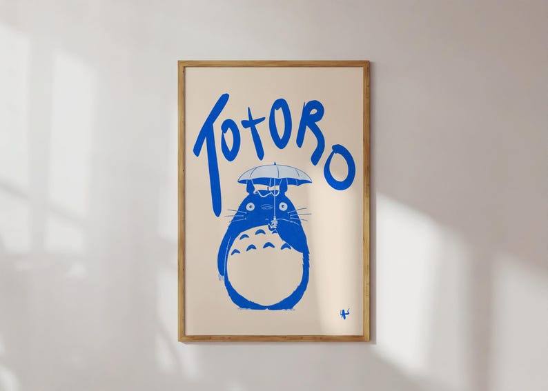 K&ouml;nnte beinhalten: Gerahmter Kunstdruck mit dem Wort "Totoro" in Blau und einer blauen Illustration der Figur, die einen Regenschirm h&auml;lt. Der Hintergrund ist hellbeige und der Rahmen aus Holz.