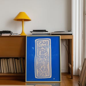 May include: A framed blue print with a list of animated film titles and years in white text. A yellow lamp with a conical shade sits on a wooden cabinet. A record player is on the cabinet.
