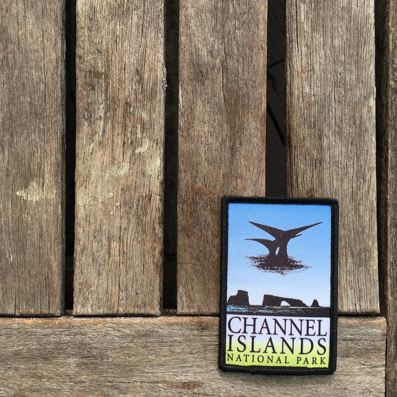 Op de afbeelding: Een zwart-witte patch met een blauwe achtergrond. De patch toont een silhouet van een eiland met een rotsboog en een vogel die erboven vliegt. De tekst "CHANNEL ISLANDS NATIONAL PARK" is gedrukt in witte letters op een groene achtergrond.