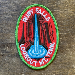May include: Oval-shaped embroidered patch with a red background and a green border. The patch features the text "RUBY FALLS LOOKOUT MT. TENN." in white, with a blue waterfall illustration.