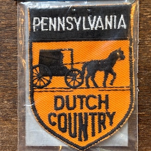 May include: A Pennsylvania Dutch Country patch featuring a black horse-drawn carriage and the words "PENNSYLVANIA" and "DUTCH COUNTRY" in white and black. The patch has an orange background.