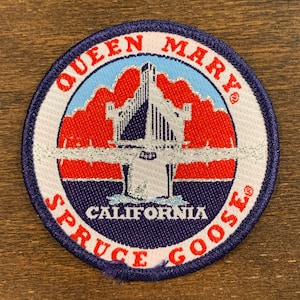 May include: A blue and white embroidered patch with the text "Queen Mary" and "Spruce Goose" in a circle around a silver and blue image of a ship. The text "California" is below the ship.